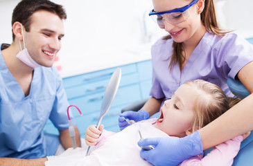 Obraz premium Little girl holding mirror at dentists