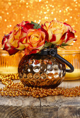 Bouquet of orange and red roses in golden vase on wooden table.
