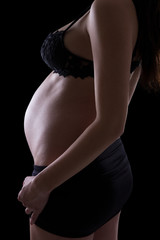 young pregnant woman in lingerie isolated on black