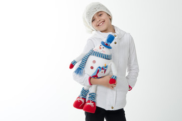 girl holding a toy snowman. Dressed in a white hat and jacket.