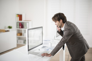 businessman at phone leaning at his computer