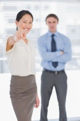 Businesswoman pointing towards the camera with man in office