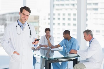 Doctor text messaging with group around table in hospital