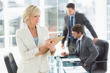 Fototapeta premium Businesswoman writing on clipboard with colleagues in background