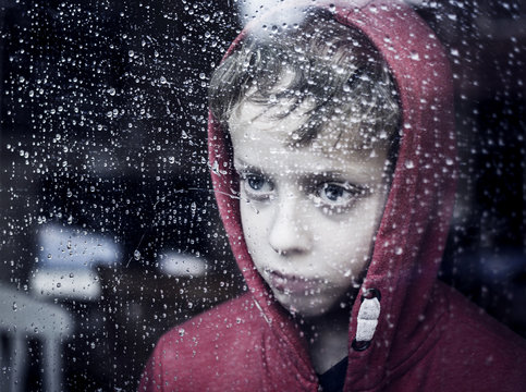 Sad Boy Looking Through Window To The Rain