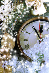 Clock with fir branches and Christmas decorations under snow