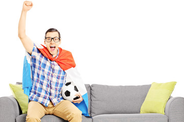 Cheerful male sport fan with soccer ball and flag watching sport