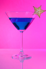 Blue cocktail in martini glass on pink background