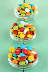 Colorful candies in glass bowls on green wooden background