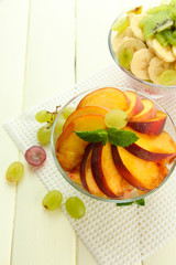 Tasty fruit salad in glass bowls, on white wooden table