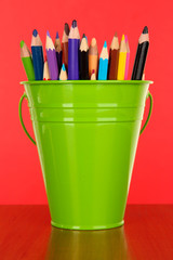 Color bucket with multicolor pencils, on color background