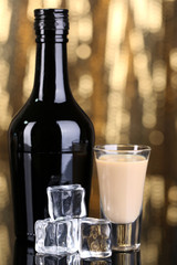Baileys liqueur in bottle and glass on golden background