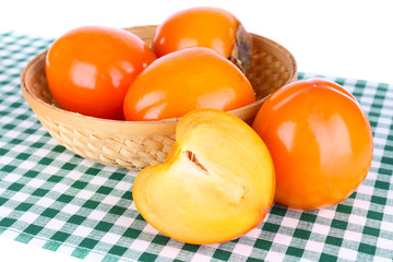 Ripe persimmons in wicker basket on table on white background