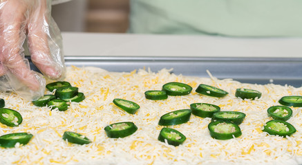 Hand laying out jalapeno, cheddar cheese for pan pizza.