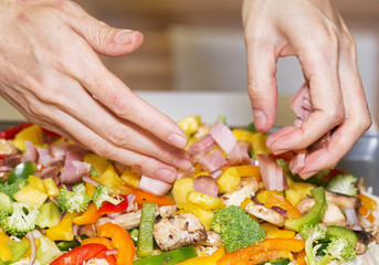 Hands arranging fresh vegetables and meat for pan pizza.