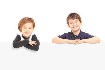 Smiling boy and girl posing behind a blank panel