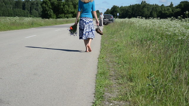 Barefoot woman with conflower bouquet walk toward car on road