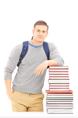 Smiling male student with school bag posing on a pile of books