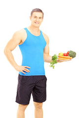 Young male athlete holding a dish full of fresh vegetables