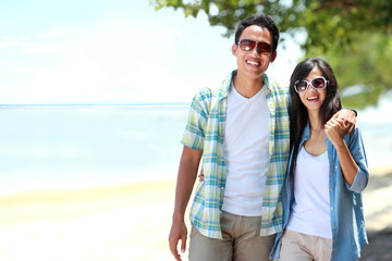 Fototapeta premium Happy couple walking by the beach together in love holding aroun