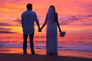 Just married couple holding hands on the beach at sunset