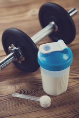 Protein shake and a dumbbell on a wooden surface