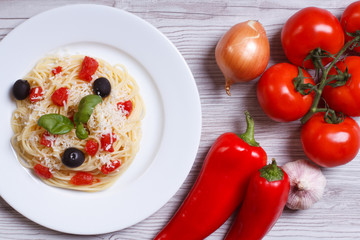 spaghetti with tomatoes, olives and ingredients on the table