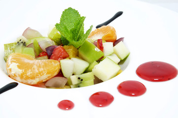 fruit salad decorated with mint on a white plate