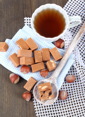 Many toffee in spoon and cup of tea on napkins on wooden table