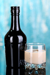 Baileys liqueur in bottle and glass on blue background