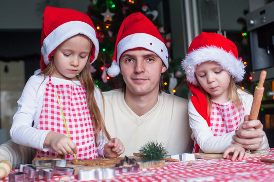 Young dad with little daughters in Santa hat bake Christmas
