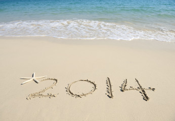 Year 2014 hand written on the white sand in front of the sea