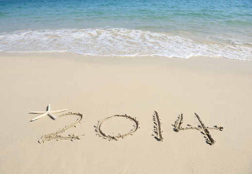 Year 2014 hand written on the white sand in front of the sea
