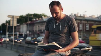 man reading book by busy city street - Powered by Adobe