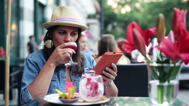 Young woman using tablet and tasting a glass of wine