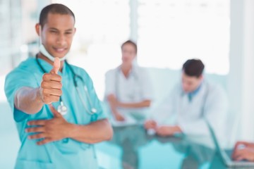 Surgeon gesturing thumbs up with group around table in hospital