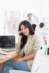 Casual woman on call at desk with colleagues behind in office