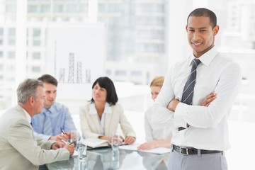 Fototapeta premium Young businessman looking at camera while staff discuss behind h