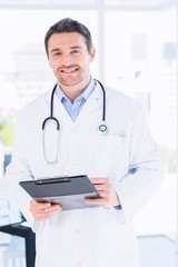 Confident male doctor with clipboard in hospital