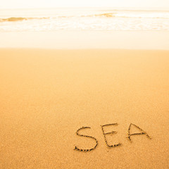 Sea, written by hand in sand on a sea beach, with a soft wave.