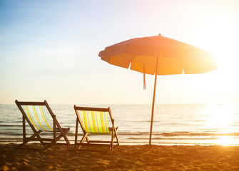 Pair of beach loungers on deserted coast sea at sunrise.