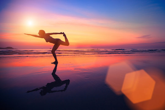 A silhouette of a woman practicing yoga on the beach at sunset.