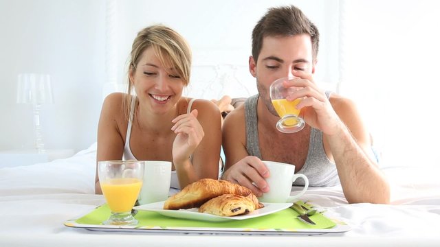 Cheerful young couple having breakfast in bed
