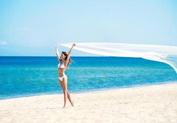 A woman in a swimsuit posing with a silk blanket on the beach