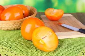 Ripe persimmons in wicker basket on table on bright background