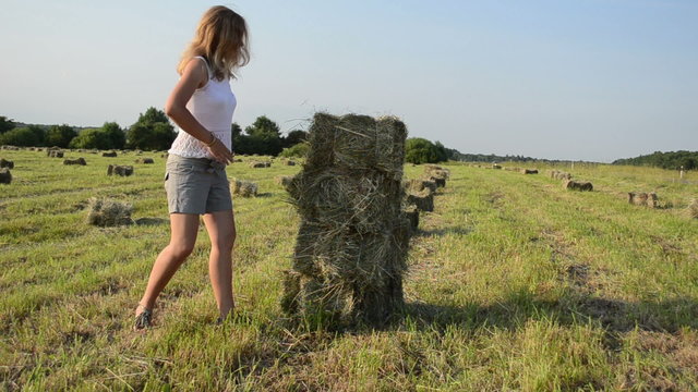 Attractive young woman dressed in short carry stack bales of hay