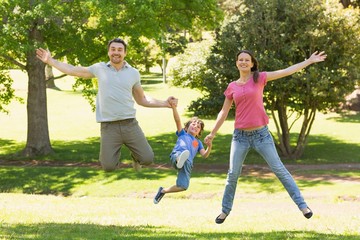 Obraz premium Family of three holding hands and jumping at park