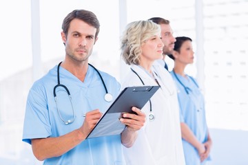 Fototapeta premium Portrait of a male doctor writing reports with colleagues behind
