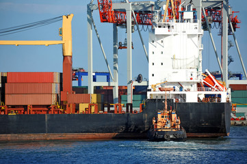 Tugboat assisting container cargo ship to harbor quayside