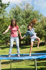 Fototapeta premium Happy girl and mother jumping high on trampoline in park